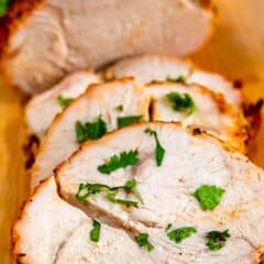 Sliced Roasted Turkey Breast garnished with fresh parsley on a wooden cutting board, featuring a larger unsliced portion in the background.