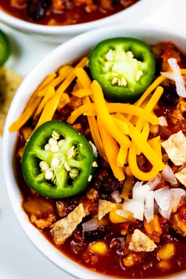Closeup shot of turkey chili in a white bowl topped with onions, cheese and jalapenos