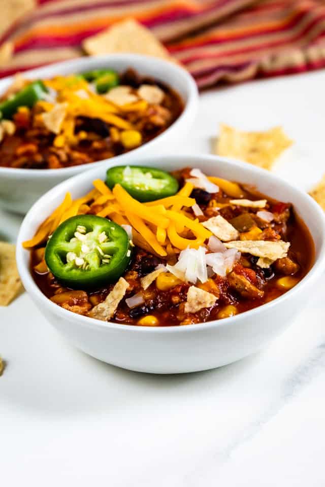 Turkey chili in two bowls with toppings and chips around the bowls