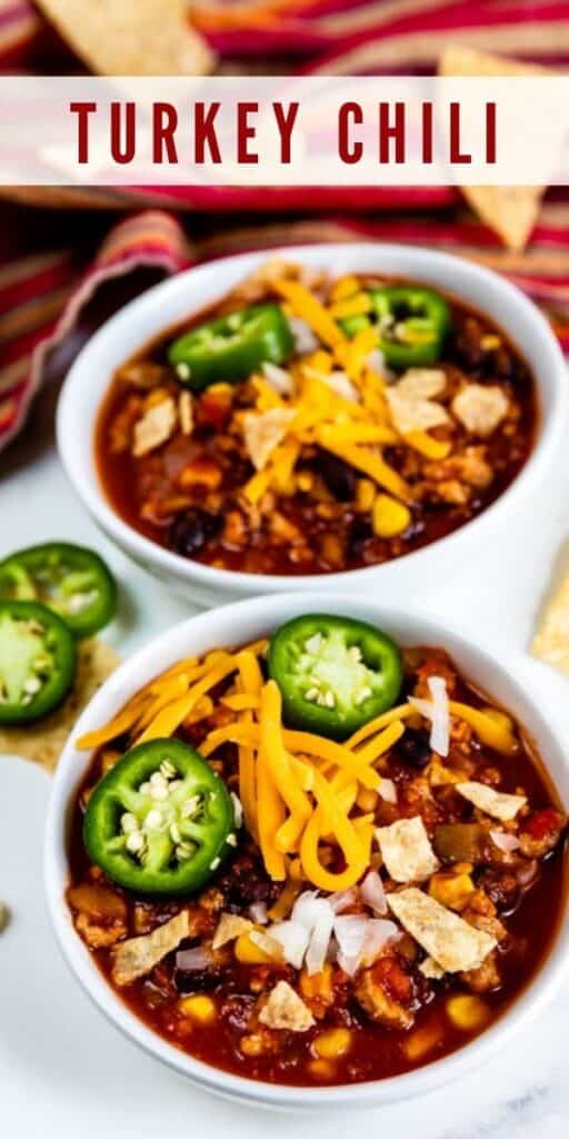 Overhead shot of two bowls filled with turkey chili and topped with cheese and jalapenos and recipe title on top of image