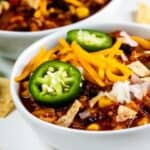 Turkey chili in two bowls with toppings and chips around the bowls and recipe title on bottom of image