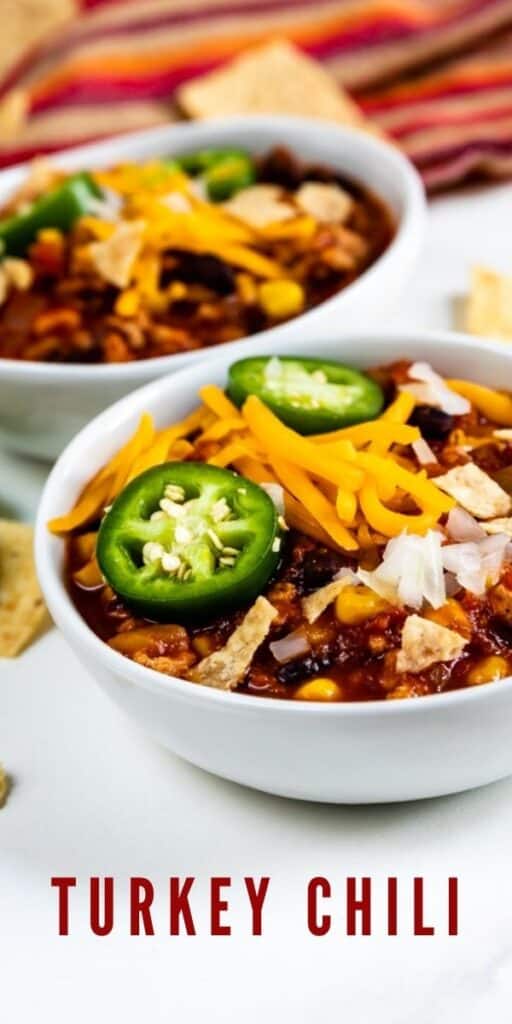 Turkey chili in two bowls with toppings and chips around the bowls and recipe title on bottom of image