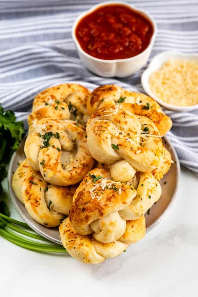 Plate full of garlic knots with dipping sauce and cheese on the side