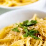 Close up photo of a bowl of garlic butter pasta with a second blurred in the background with recipe title on top of image