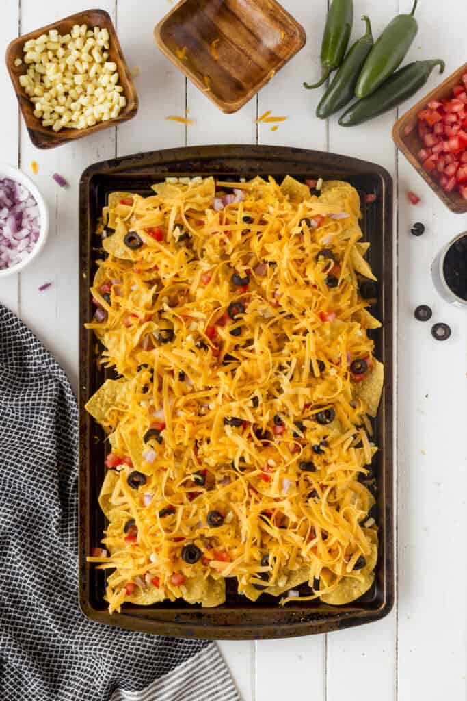 Overhead shot of nachos on a sheet pan surrounded by different nacho toppings