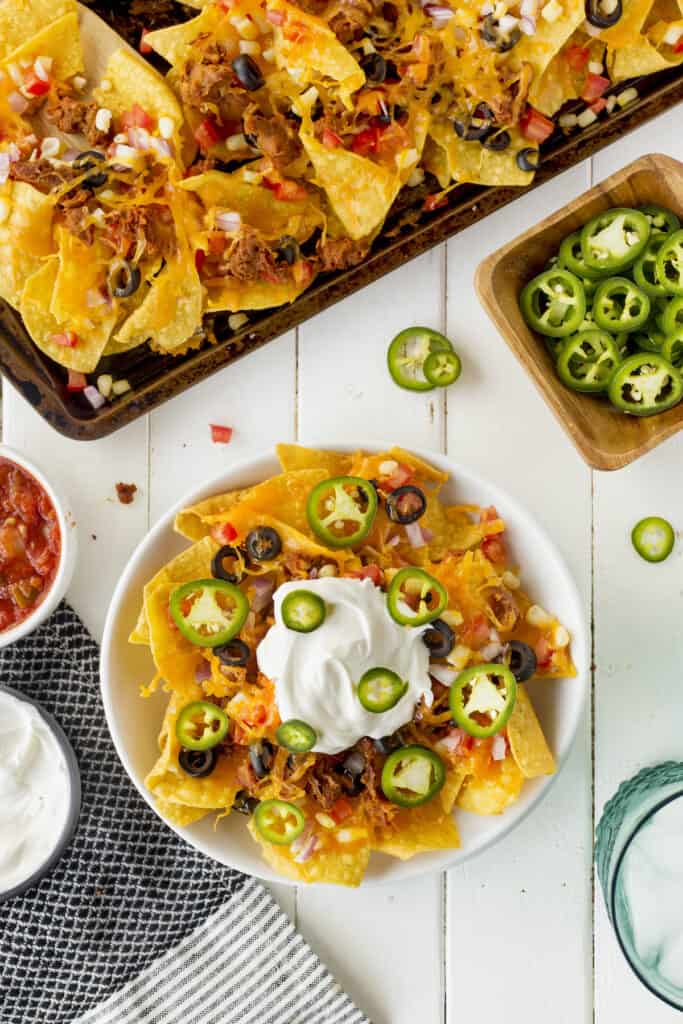 Overhead view of plate of vegetarian sheet pan nachos with toppings and full sheet pan in background