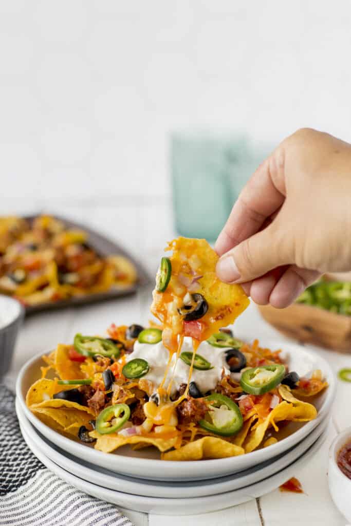 Plate full of vegetarian sheet pan nachos with hand pulling one off plate