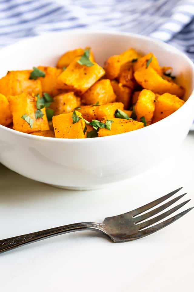 Roasted butternut squash cut into cubes and placed in a bowl topped with herbs