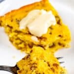 Slice of sausage cornbread with a pat of butter on top on white plate with one bite on fork and recipe title on top of image
