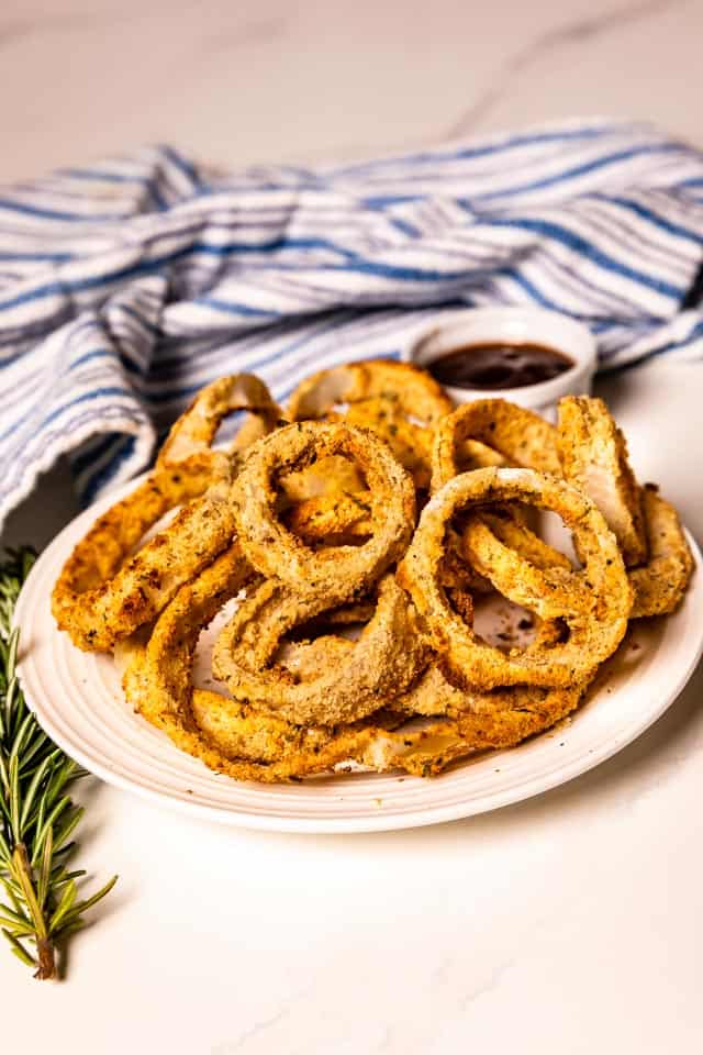 Air fryer onion rings on a white plate with dipping sauce on the side