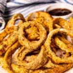 Air fryer onion rings on a white plate with dipping sauce on the side and recipe title in top right corner