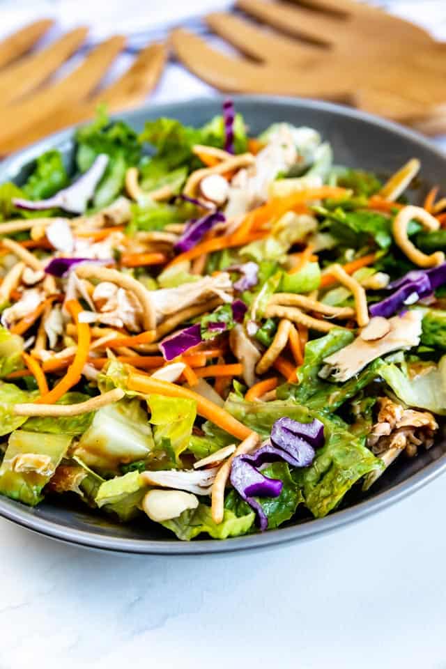 Bowl of chinese chicken salad with wooden serving forks in background and recipe title on bottom right of image