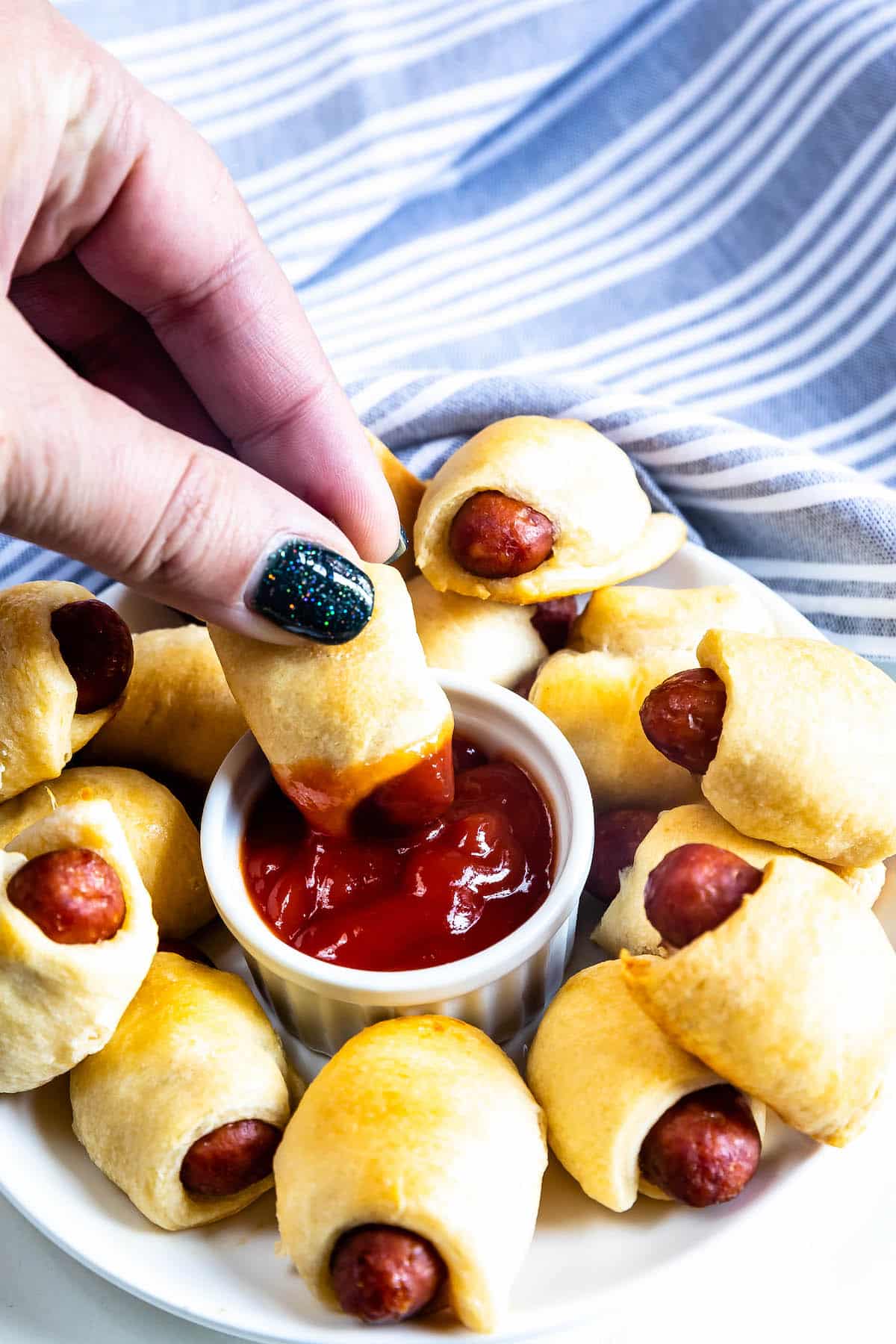 plate of pigs in a blanket with hand dipping in ketchup