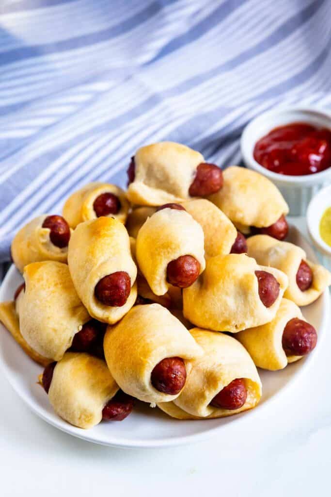 Plate stacked high of pigs in a blanket with dipping sauces behind it