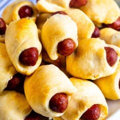 Close up shot pigs in a blanket stacked high on a plate with dipping sauces behind it