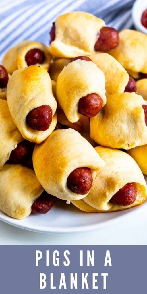 Close up shot pigs in a blanket stacked high on a plate with recipe title on bottom of photo