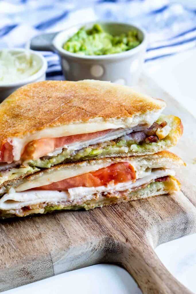 Turkey Avocado Bacon Panini cut in half and stacked on a wooden cutting board