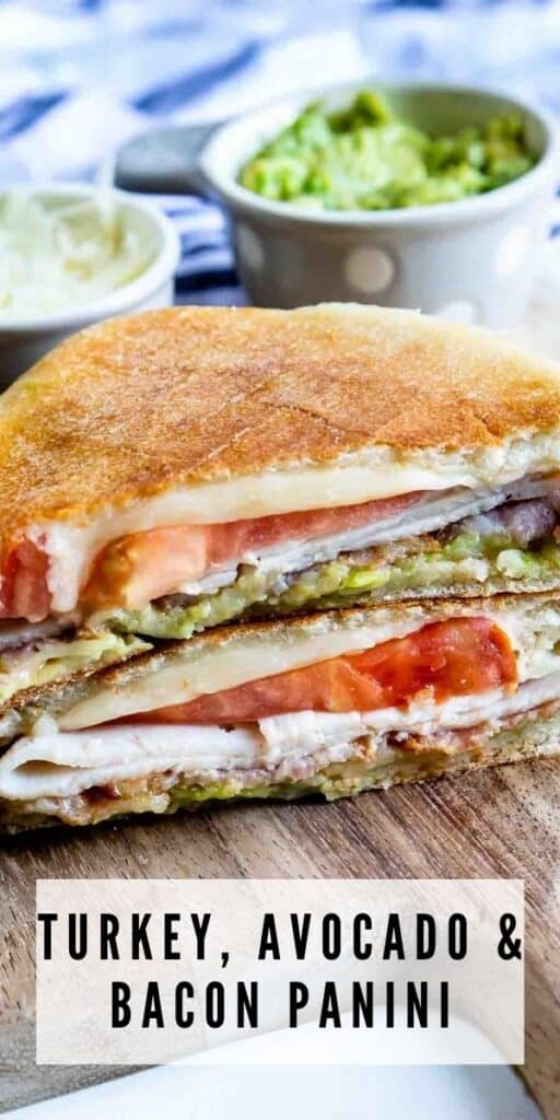 Turkey Avocado Bacon Panini cut in half and stacked on a wooden cutting board with recipe title on bottom of image