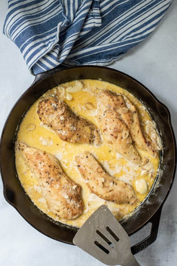 Overhead shot of chicken in garlic sauce in cast iron skillet with blue dish towel on the side