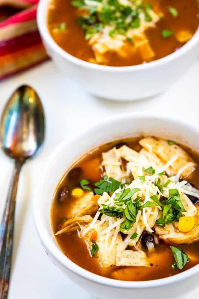 Two bowls of easy chicken tortilla soup with spoon next to bowl