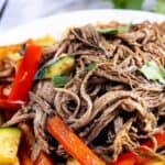 Crockpot flank steak on a plate with veggies and recipe title on top of image