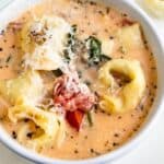 Overhead shot of tortellini soup in a white bowl with recipe title on bottom of photo