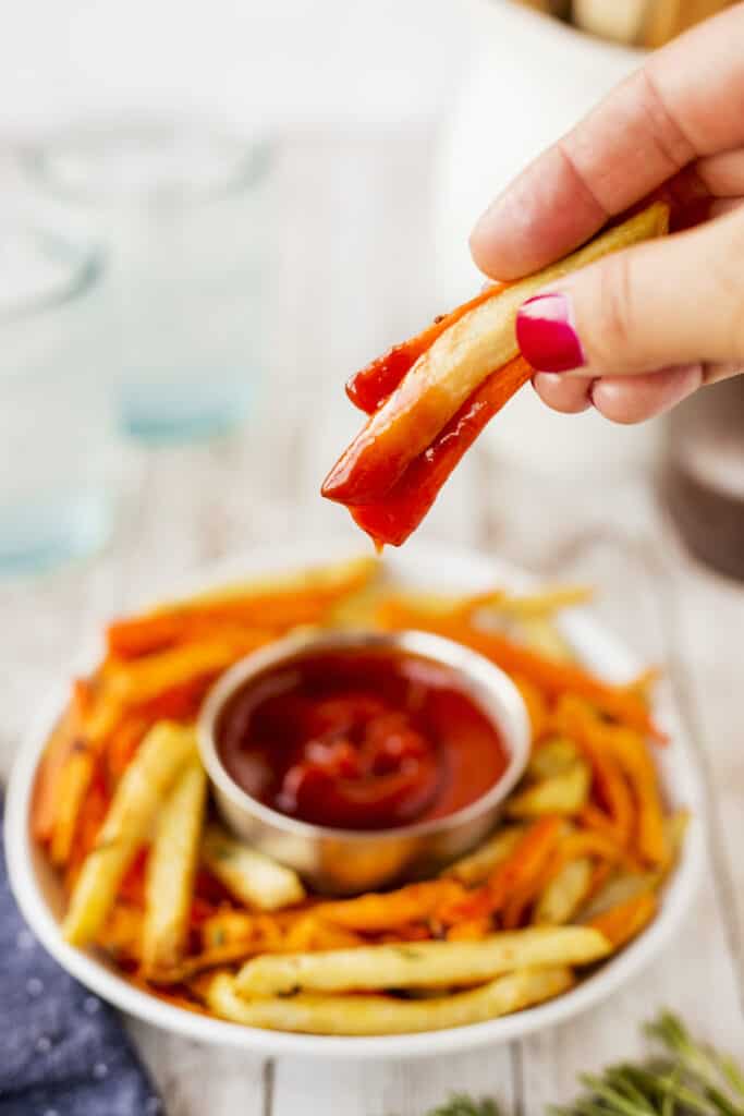 Air fryer fries being held in a hand after being dipped in ketchup