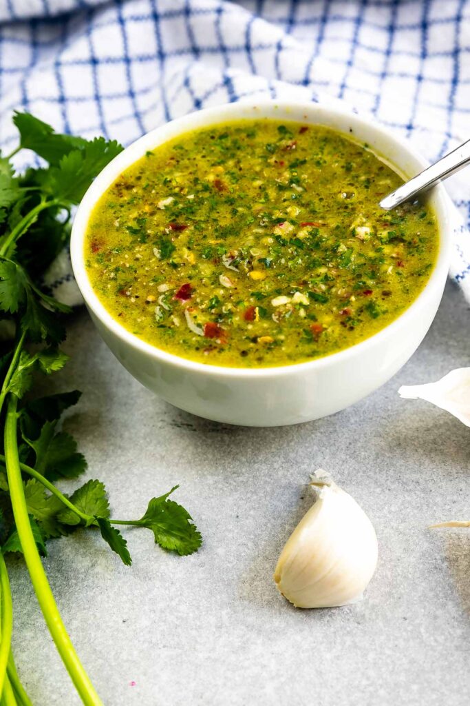 Overhead shot of a bowl of chimichurri sauce with ingredients around it