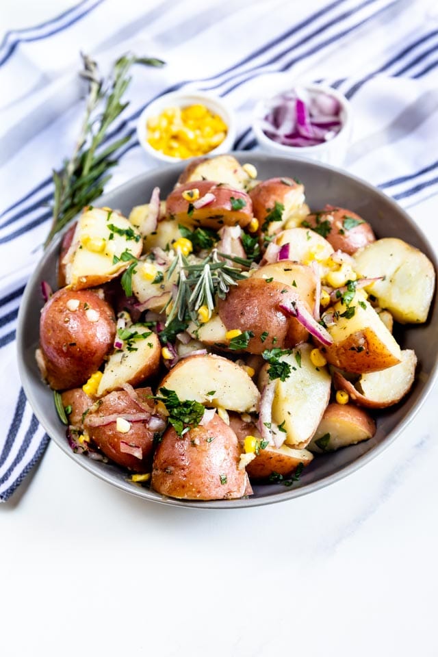 Bowl full of garlic herb potato salad with herbs and other ingredients around it