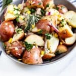 Bowl full of garlic herb potato salad with herbs and other ingredients around it and recipe title on bottom of image