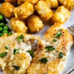 Close up shot of pan seared cod with sides of tater tots and peas