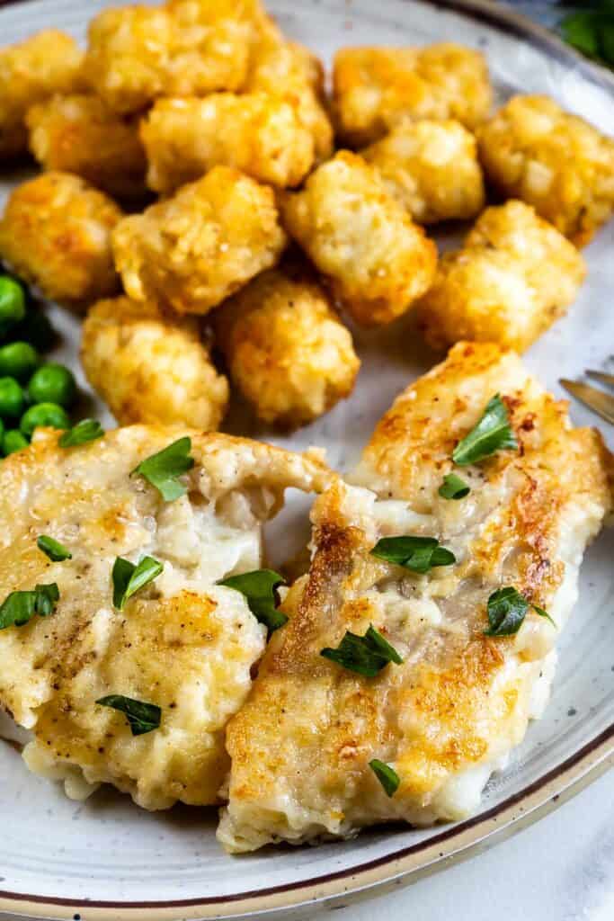 Close up shot of pan seared cod with sides of tater tots and peas