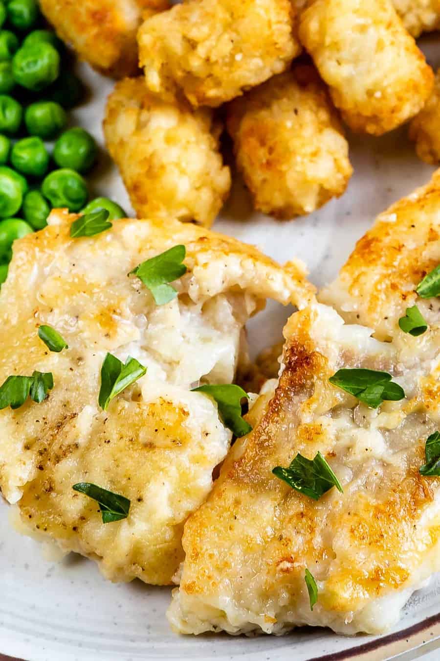 Close up shot of pan seared cod with sides of tater tots and peas