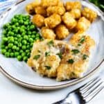 Pan seared cod on a plate served next to peas and tater tots with recipe title on bottom of photo
