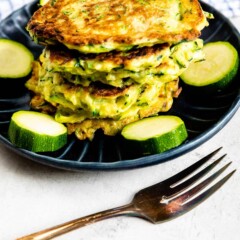 Stack of zucchini fritters on a plate surrounded by circled zucchinis