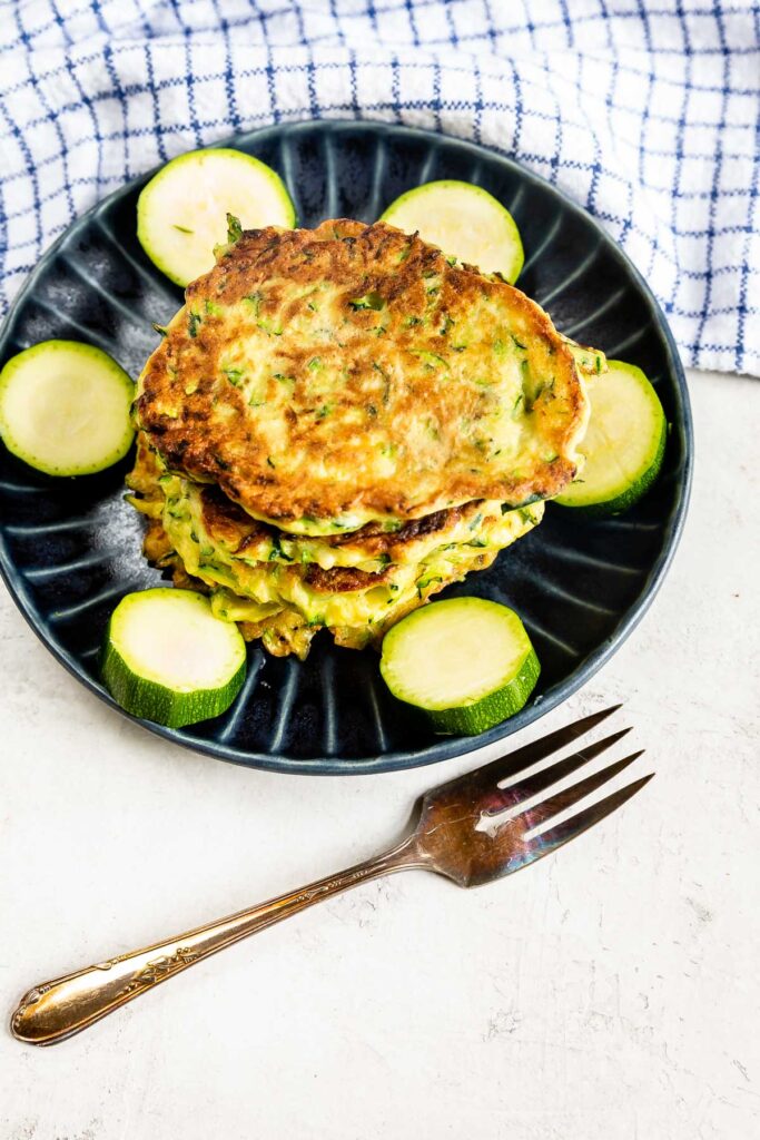 Overhead shot of zucchini fritters on a plate surrounded by zucchini pieces