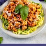 Plate full of zucchini noodles topped with meat sauce and basil with recipe title on bottom of photo