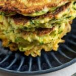 Stack of zucchini fritters on a blue plate with a fork next to it and recipe title on bottom of photo