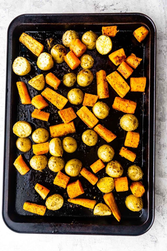 Overhead shot of roasted potatoes and carrots on a black sheet pan