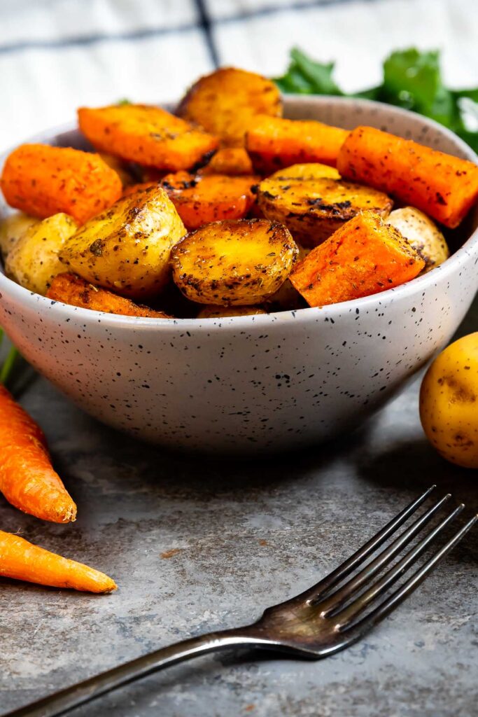 Bowl full of roasted potatoes and carrots with a fork in front of it