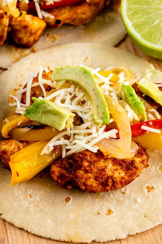 Close up of tortilla filled with sheet pan chicken fajitas, peppers, cheese and avocado
