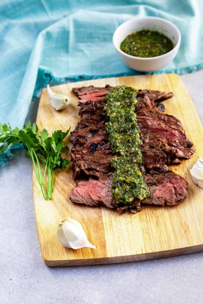 Sliced skirt steak on a cutting board with chimichurri sauce on top