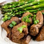 Plate full of air fryer steak tips with asparagus with recipe title on bottom of image
