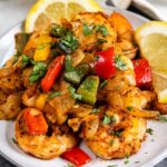 Plate full of cajun shrimp with bell peppers and fresh lemon slices