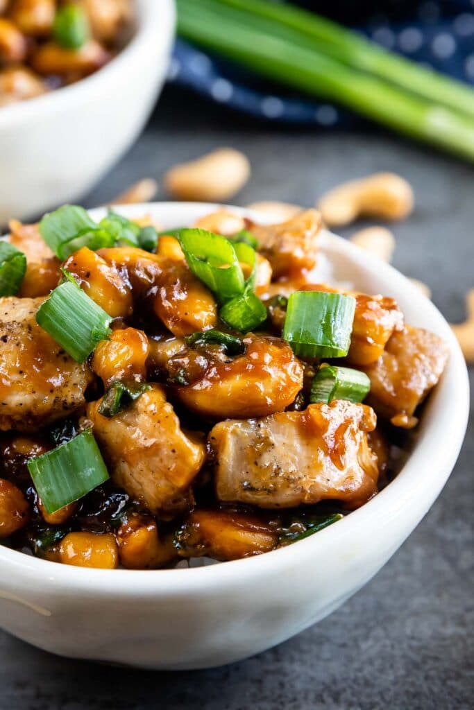Side shot of cashew chicken in a bowl topped with green onions
