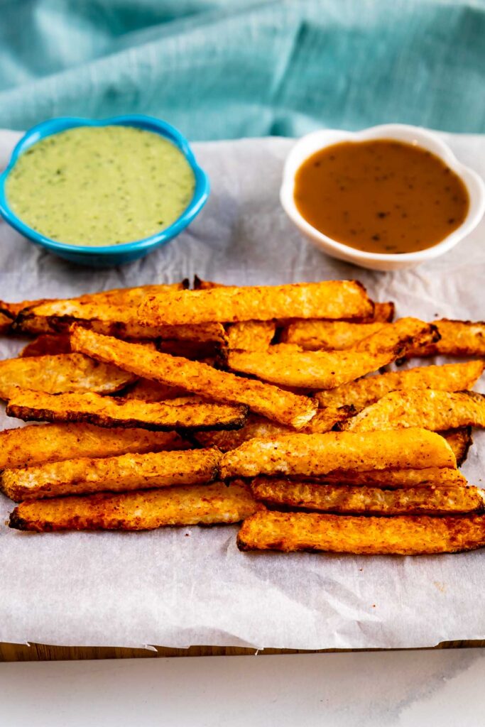 Jicama Fries on parchment paper with dipping sauces behind them