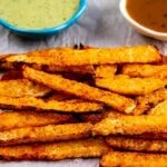 Jicama Fries on parchment paper with dipping sauces behind them and recipe title on bottom of photo