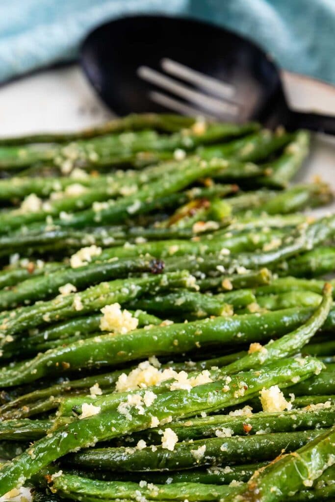 Close up shot of roasted green beans on a serving plate with serving spoon