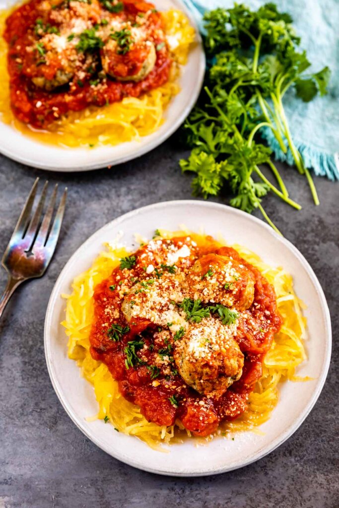 Two plates of spaghetti squash and meatballs topped with cheese and herbs