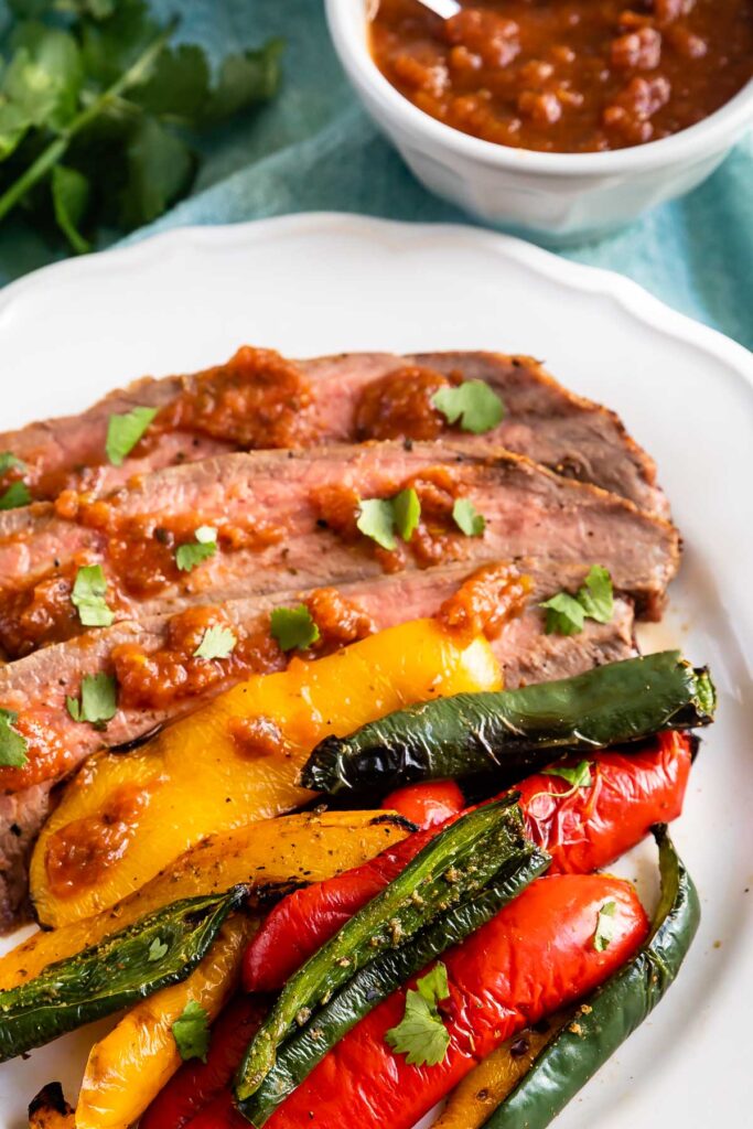 Steak and peppers on a plate with sauce behind it